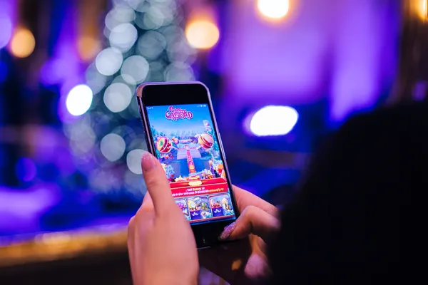 একজন তরুণী তার ফোনে আরাম করে গেম খেলছেন, আর চারপাশে ভাসছে ডায়নামিক ক্যাসিনো উপাদান—যা BAJI200 অ্যাপের মসৃণ মোবাইল অভিজ্ঞতাকে ফুটিয়ে তোলে।